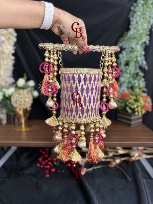 Royal purple handcrafted wedding potli with golden zari lattice embroidery, pink tassels, embellished handle and decorative latkans.